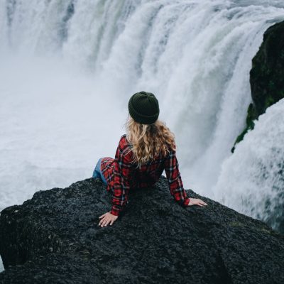 Woman sit on edge of cliff on waterfall